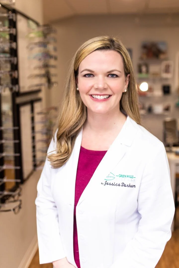 A woman in white lab coat standing next to glasses.